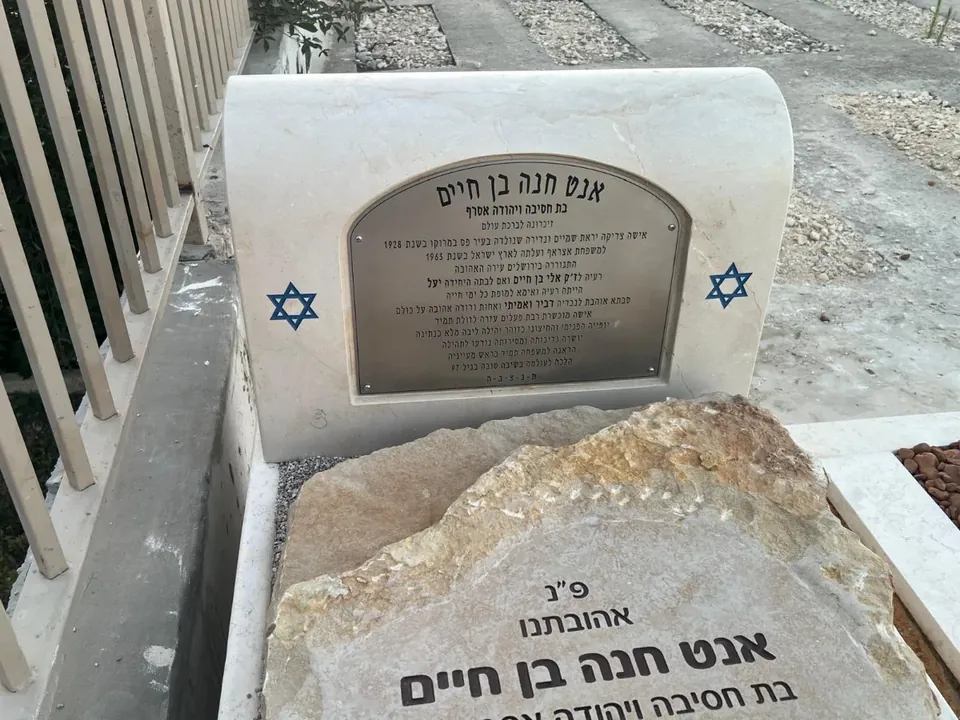 שלט מתכת מותקן על מצבת אבן בבית עלמין, עם כיתוב בעברית ושני מגני דוד